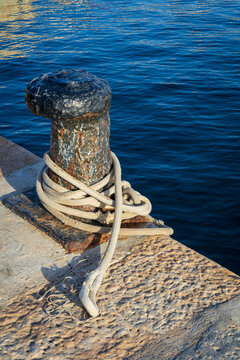rusty mooring bollard with rope on harbor dock