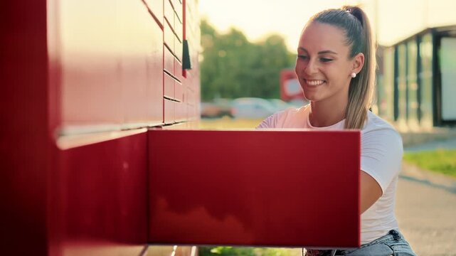 Young smiling woman placing a cardboard box into a self-service parcel locker for shipping