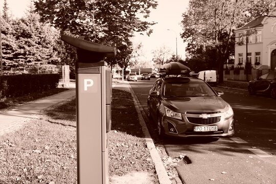 Sepia-toned street scene with a Chevrolet parked beside a curbside parking meter in Poznan