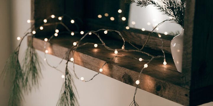 Warm white string lights on a rustic shelf with pine branches and a vase