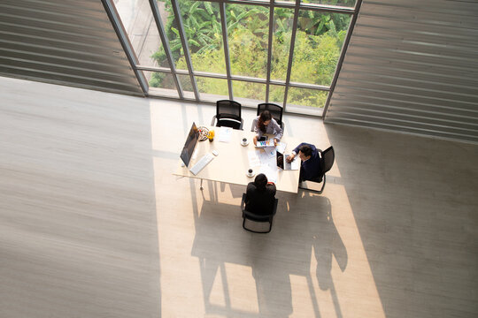 Top view of diverse business people meeting around a table near large glass windows in a modern corporate office, planning financial strategy, teamwork collaboration, and executive brainstorming