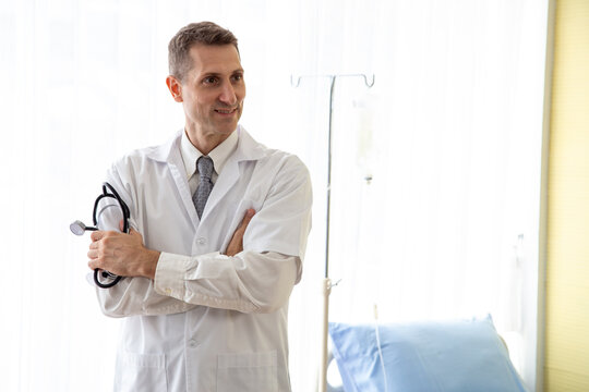 Confident Caucasian male doctor standing arms crossed holding a stethoscope in a modern hospital room, offering professional healthcare service, medical treatment, and specialized patient care