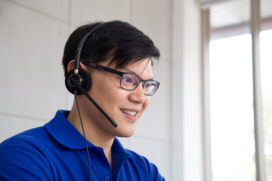 Smiling Asian male customer service operator wearing headset and glasses, providing professional online support, telemarketing hotline, helpdesk consultation, and call center client assistance