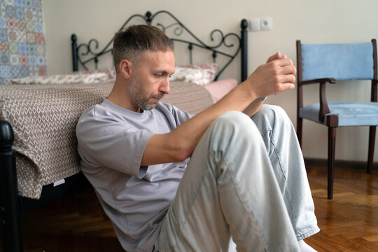 Midlife crisis and loneliness leave anxious man sitting alone on bedroom floor, reflecting on difficult life decisions and uncertain future.