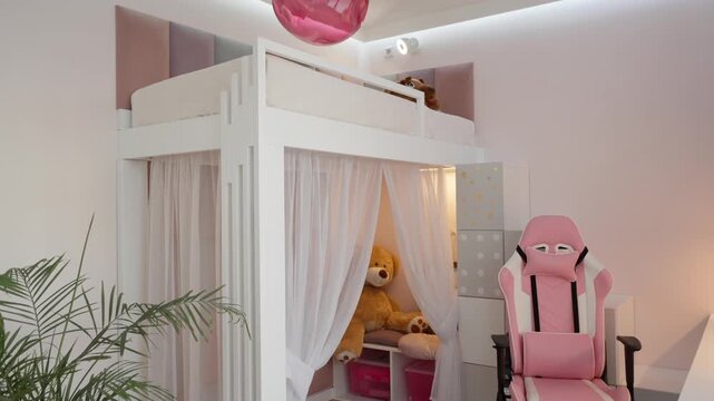White wooden loft bed features sheer canopy curtains creating a cozy play tent with a teddy bear. Pink gaming chair and soft wall panels furnish the modern girl bedroom.