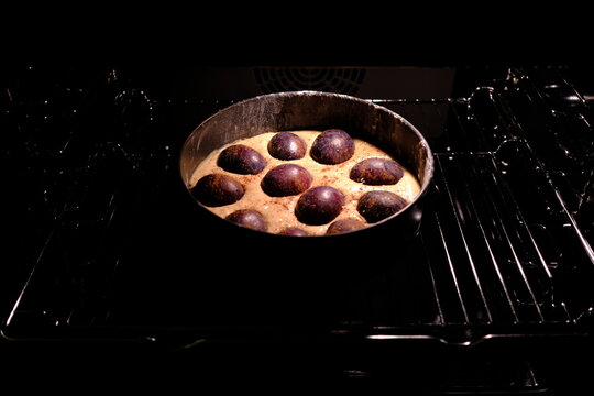 Homemade plum pie topped with whole plums and cinnamon in a round springform pan, ready to bake in the oven, cozy autumn baking