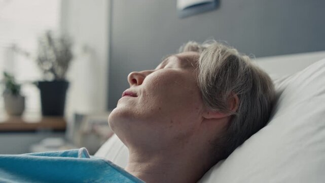 Middle aged Caucasian woman lying on pillow in hospital bed, slowly regaining consciousness. Footage suitable for medical recovery narratives and clinical healthcare promotions