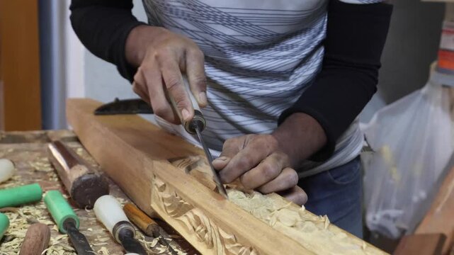 View of a skilled craftsman using a chisel to carve intricate patterns into wood for a traditional dhow boat in a workshop in Sur, Ash Sharqiyah South G, Oman.