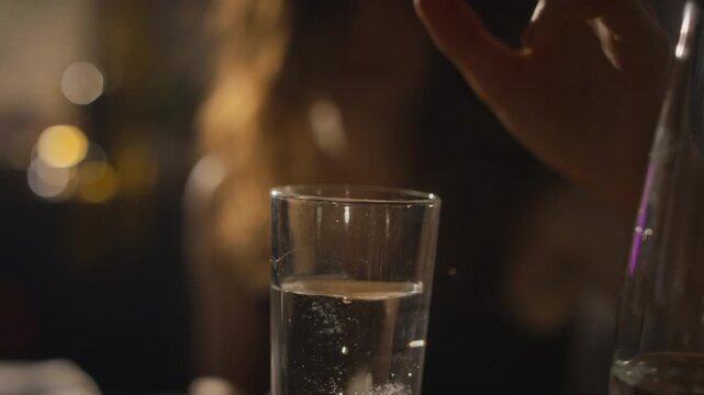 Caucasian young adult woman dropping effervescent tablet into glass of water and drinking dissolved remedy. Suitable for hangover relief, dietary supplements, and healthcare campaigns