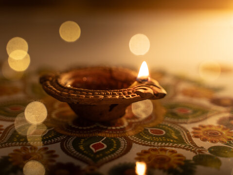 Traditional Clay Diya Lamp Glowing with a Warm Flame Placed on a Colourful Hand-Made Rangoli Design.
