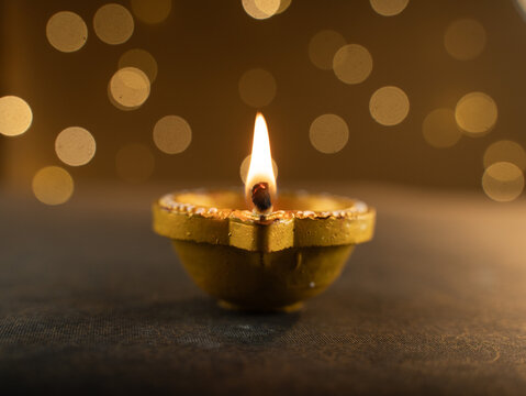 Four Traditional Clay Diwali Diyas with Flickering Flames Arranged on an Ornate Golden Patterned Surface, Warm Festive Close-Up Shot.