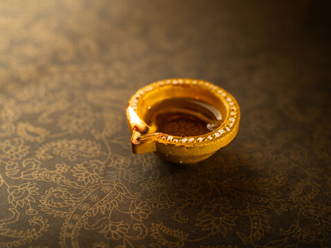 Traditional Clay Diwali Diyas with Flickering Flames Arranged on an Ornate Golden Patterned Surface, Warm Festive Close-Up Shot.