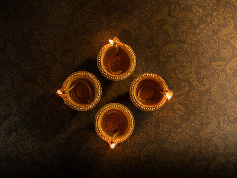 Four Traditional Clay Diwali Diyas with Flickering Flames Arranged on an Ornate Golden Patterned Surface, Warm Festive Close-Up Shot.