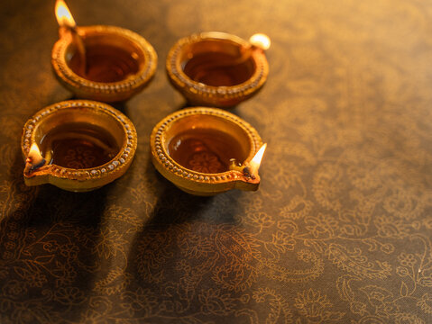 Four Traditional Clay Diwali Diyas with Flickering Flames Arranged on an Ornate Golden Patterned Surface, Warm Festive Close-Up Shot.