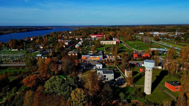 Aerial view of the town of Lielvarde featuring a prominent water tower, surrounded by autumn trees and a nearby river in Lielvarde, Ogre Municipality, Latvia.