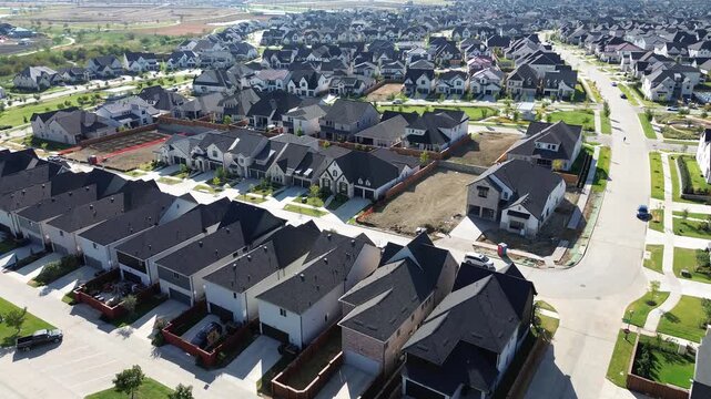 Curved residential streets border densely grouped single family homes dark shingle roofs along Frisco. Graded land parcels await concrete foundation pouring across expanding suburban, Texas