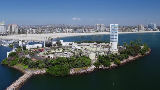 Aerial view showcases THUMS Island Grissom in Long Beach harbor, California, displaying disguised oil drilling structures, palm trees, and the coastal city skyline under bright sunshine.