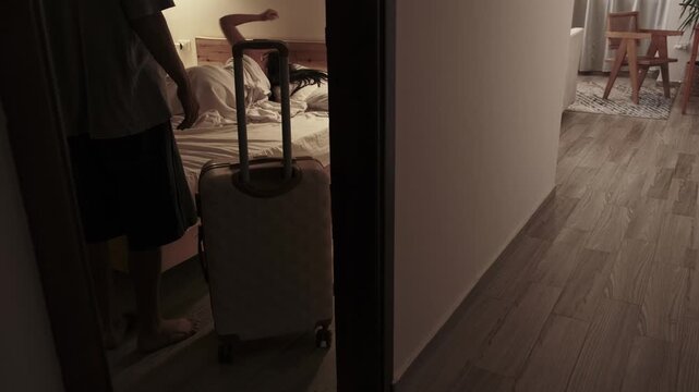 Woman waving goodbye and turning away from her partner while he stands beside a suitcase watching silently, portraying emotional detachment, relationship conflict and separation at home