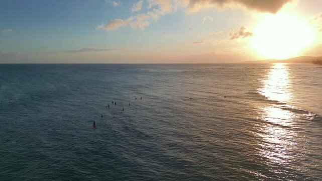 Distant surfers wait on gentle ocean swells beneath warm sunset reflections.