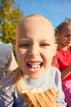 Laughing little girl holding ice cream cone in sunny park closeup with joy. Childhood happiness, carefree leisure concept.