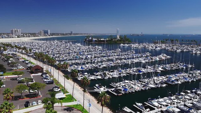 Aerial view displays hundreds of yachts and sailboats docked in Long Beach Shoreline Marina, featuring palm trees, a parking lot, and THUMS Island Grissom under clear skies.