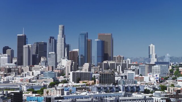Aerial perspective across the downtown Los Angeles skyline with prominent financial towers and urban architecture set against clear daytime skies in California.