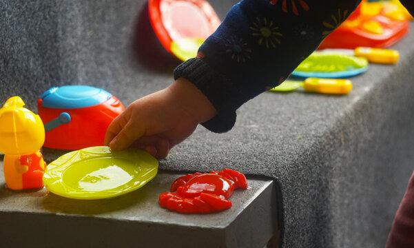 Child hand playing with plastic toy kitchen utensils indoors.