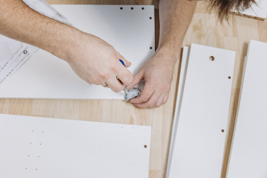 Close up hands of man assembling white wooden furniture tightening screw with tool DIY home assembly project craftsmanship