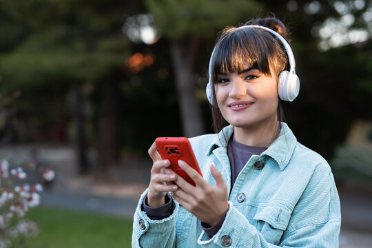 Young woman smiling enjoying music with smartphone outdoors