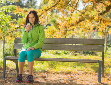 Woman Listening to Music with Headphones on a Park Bench in Autumn