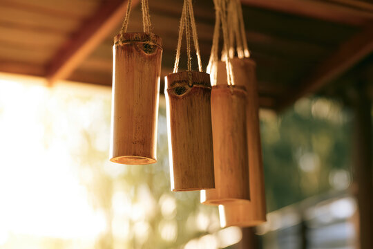 Bamboo wind chime suspended from wooden porch overhang with warm sunlight and gentle motion, creating serene acoustic mindfulness scene with natural texture and space for copy