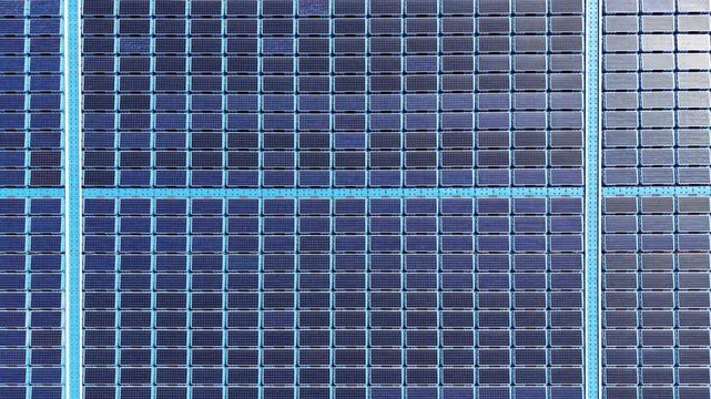 Overhead view of rows of blue photovoltaic solar panels arranged in a grid, showing cells and busbars for renewable energy generation