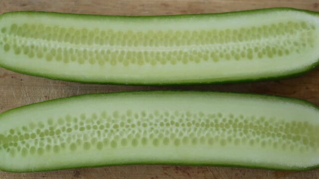 Top view close up of fresh green cucumber sliced in half lengthwise on wooden surface