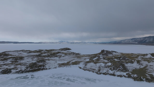 An elevated winter view captures Lake Baikal beside Maloye More, where snow-covered ridges frame the icy shore under a subdued sky in Irkutsk Oblast, Russia, across Siberia's open landscape