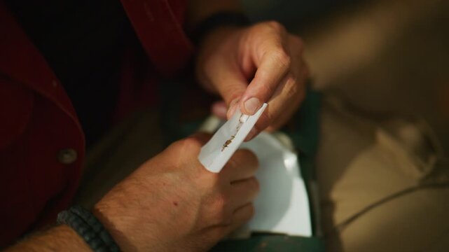 Hands roll a tobacco cigarette, placing loose tobacco in rolling paper and tucking it by hand in a static close-up.