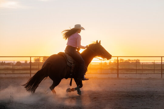 White woman riding horse in corral at sunset on a ranch