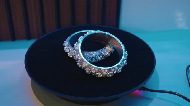 Pair of decorative bangles placed on a motorized rotating display turntable with blue neon studio lighting