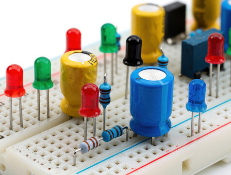 Close up view of electronic components on white breadboard. Colorful led lights, resistors, capacitors installed for circuit prototype. Hardware parts used in electrical engineering, school science
