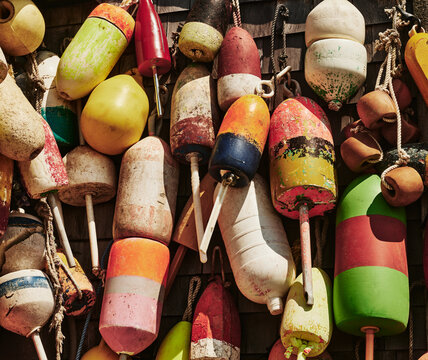 weathered, colorful lobster buoys hanging against a rustic wooden shingle wall in Maine, New England