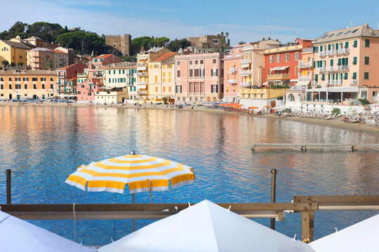 Scenic bay Sestri Levante Italian Riviera yellow umbrella sea view. Coastal lifestyle colorful buildings summer calm serene water. Tourism advertising holiday booking luxury hospitality promotion.