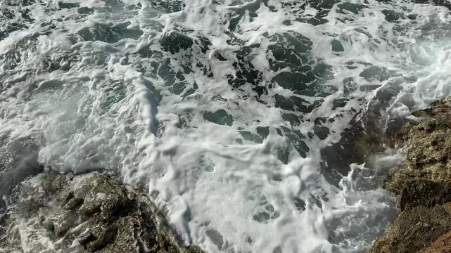 Overhead View of White Sea Foam Swirling in Water by Brown Rocks