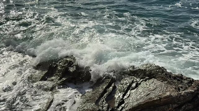 Sunlit Sea Waves Crashing on Wet Grooved Coastal Rocks with Spray