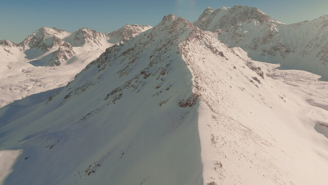 An elevated winter view captures the snowbound ridges of Przhevalsky Peak near Karakol, Issyk-Kul Region, Kyrgyzstan, where rugged alpine slopes rise against a clear sky over high terrain