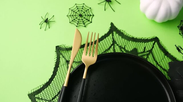 Halloween table setting with black plate and gold cutlery on green background