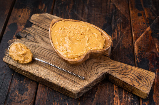 Creamy peanut butter spread in heart shaped wooden bowl on rustic cutting board with spoon. Natural peanut paste made from roasted peanuts