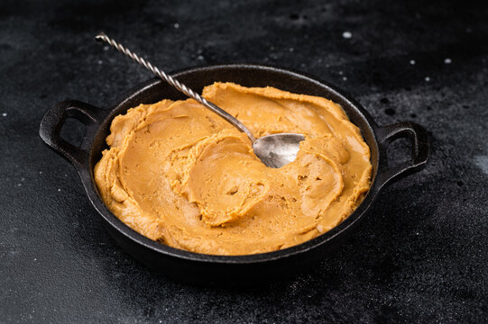 Creamy peanut butter in bowl with spoon on dark background. Natural peanut paste spread made from roasted peanuts with copy space