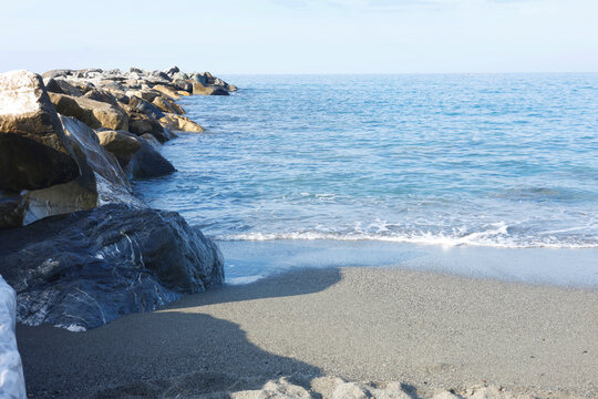 Stone breakwater rocks sea waves Sestri Levante sandy beach coast. Marine geology coastal protection calm blue water horizon. Oceanography natural science earth conservation publishing.