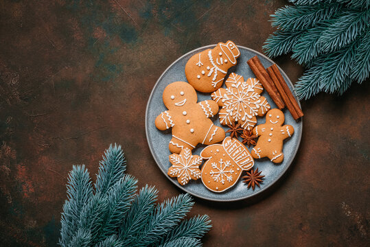 Christmas gingerbread cookies on a plate and decorative spruce branches on a dark rustic background, top view, flat lay, copy space.