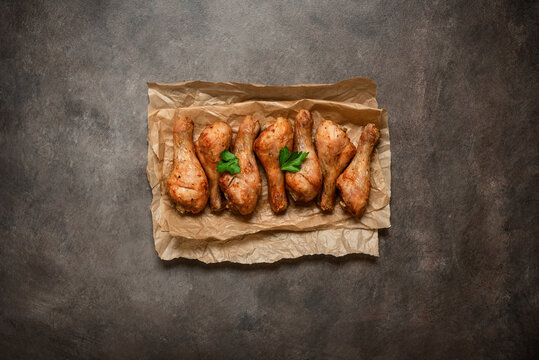 Roasted chicken drumsticks on paper, dark rustic background,close-up, top view, flat lay, copy space