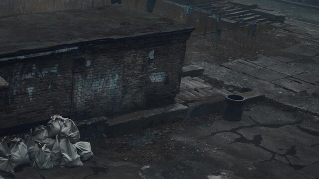 An empty urban space with cracked asphalt. Debris is scattered around, adding to the abandoned look of the area. A trash can is visible beside piles of waste.